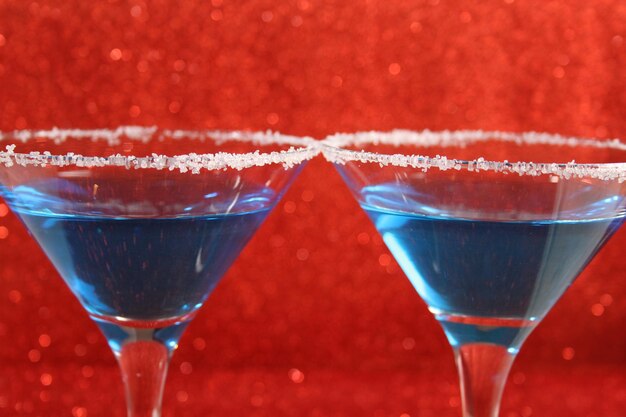 Deux verres avec des boissons alcoolisées bleues se tiennent sur un fond rouge brillant