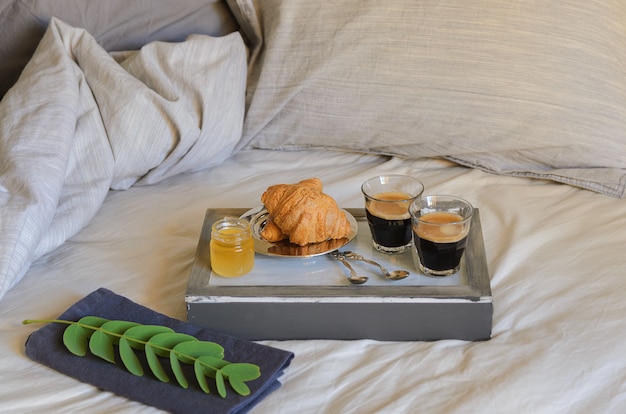 deux verres à café, croissants et confiture sur le lit