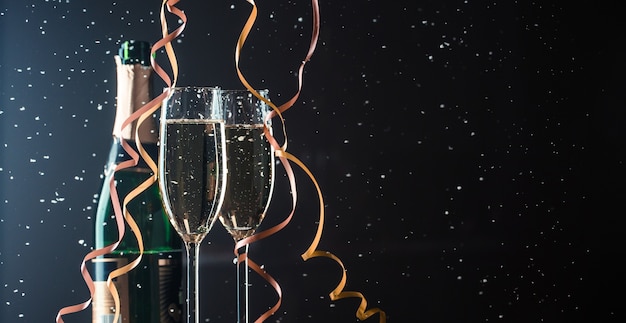 Deux verres de champagne et une bouteille sur fond sombre avec des chutes de neige. Image avec espace de copie