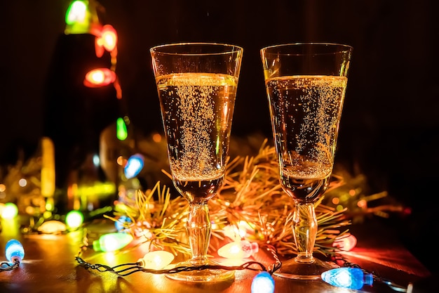 Deux Verres De Champagne Et Une Bouteille Sur Une Table En Bois Décorée D'accessoires De Noël Pour Célébrer Le Nouvel An Et Noël. Soirée Romantique. La Lueur Des Guirlandes. La Saint-valentin