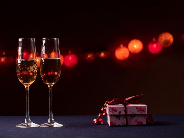 Deux verres de champagne et un cadeau rose avec un ruban rouge sur fond noir avec lumière