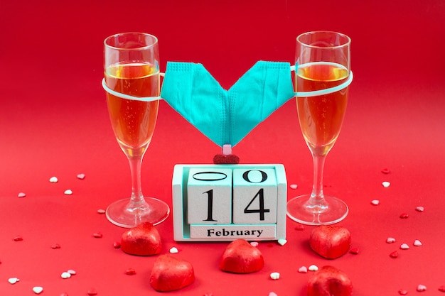 Photo deux verres à champagne, calendrier en bois, bonbons et masque médical saint-valentin sur rouge.