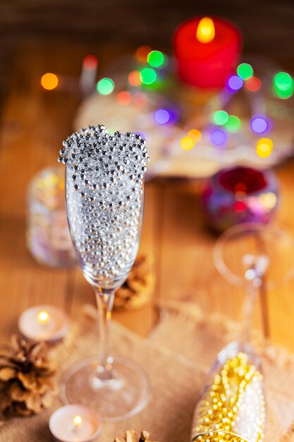 Deux verres de champagne avec des perles de Noël. Décorations de Noël dans un style rustique sur fond clair avec des lumières. Pommes de pin et bougies allumées sur le bokeh de fond