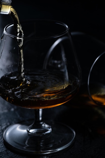 Deux verres de cognac sur fond sombre Le cognac est versé dans un verre d'en haut