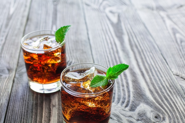 Deux verres de cola avec de la glace et de la menthe fraîche sur une belle table en bois.