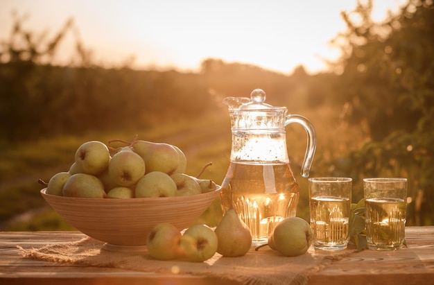Deux verres avec du jus de poire et un panier de poires sur une table en bois avec fond de verger naturel à la lumière du coucher du soleil Composition de fruits végétariens