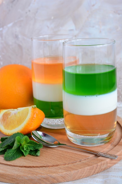 deux verres avec du lait de kiwi et de la gelée d'orange sur la planche à découper en bois