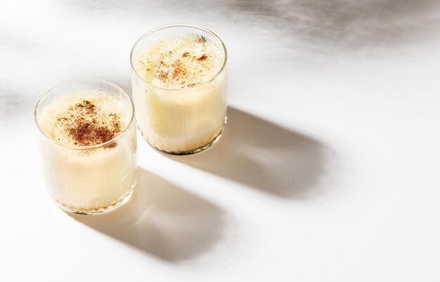 Deux verres avec du lait de poule de Noël à la cannelle sur blanc avec de belles ombres Mise au point sélective