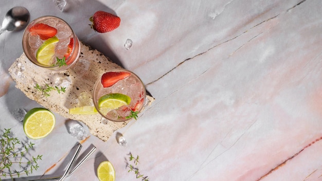 Deux verres avec du soda aux fraises fraîches boivent du thym citron vert glacé sur un podium en travertin sur fond de marbre rose