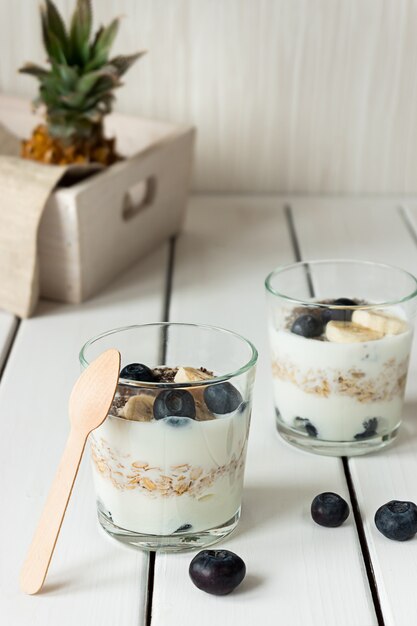 Deux verres avec du yogourt en couches d'avoine et de fruits sur une table en bois blanc Petit-déjeuner sain concept de mode de vie sain