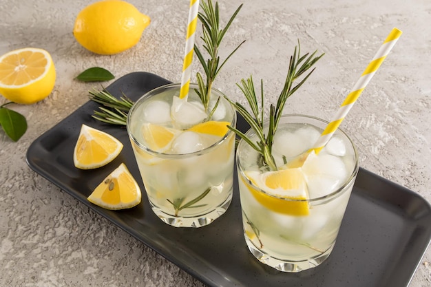 Deux verres d'eau vitaminée aux agrumes sur un plateau en céramique sombre avec des tranches de citron et de l'eau de désintoxication au romarin