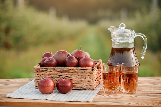 Deux verres de jus de pomme et panier de pommes sur une table en bois avec fond de verger naturel Composition de fruits végétariens
