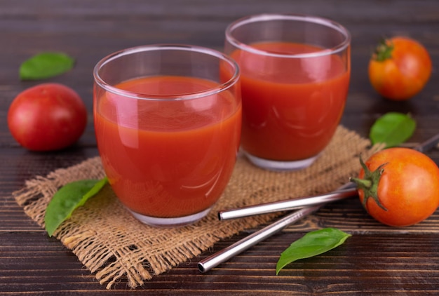 Deux verres de jus de tomate sur un fond en bois foncé.