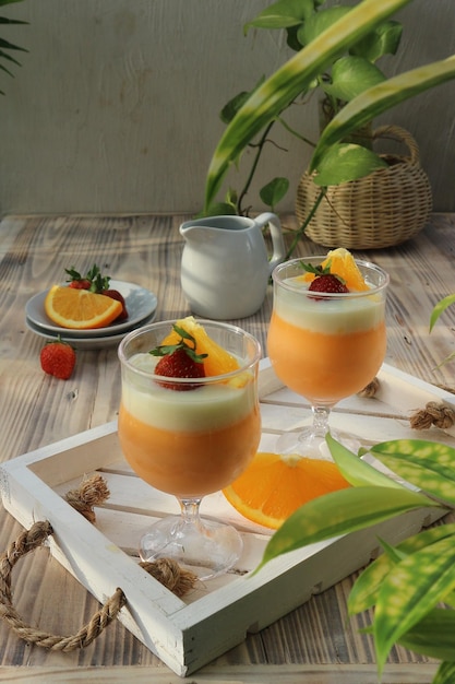 Deux verres de smoothie orange et fraise sur un plateau avec une tasse de jus d'orange.