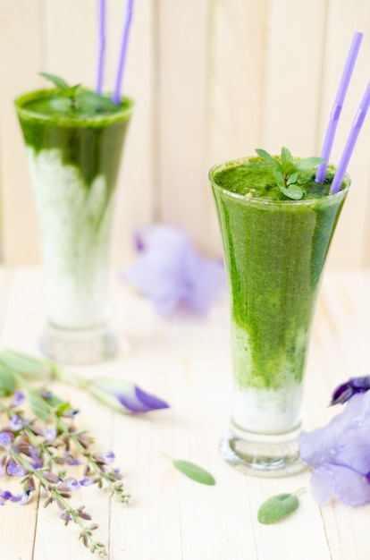 Deux verres de Smoothie vert sain avec des épinards, des kiwis et des oranges sur une table en bois clair