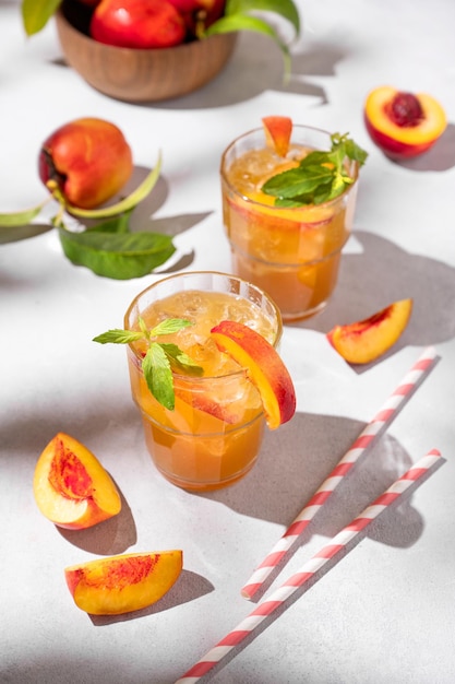 Deux verres de thé rafraîchissant à la pêche avec de la glace et de la menthe Boisson d'été froide faite maison sur un fond clair avec des fruits frais et des ombres