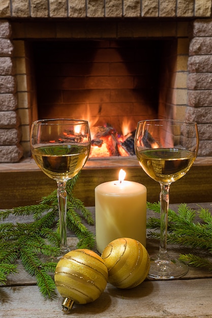 Deux verres de vin blanc, bougie, boules de verre jaune, près de la cheminée