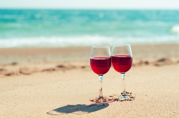 Deux verres à vin avec du vin rouge sur le sable de la plage au bord de la mer Couple romantique