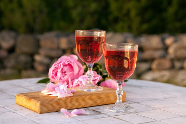 Deux verres à vin rose et bouquet de pivoine rose. délicieuse boisson rafraîchissante, énormes fleurs épanouies à table au coucher du soleil