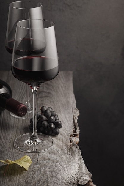 Deux verres de vin rouge, une bouteille et des raisins sur une vieille table en bois. Fond sombre.