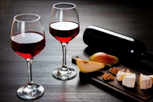 Deux verres de vin rouge et une bouteille de vin, fromage, poires, noix sur une planche à découper en bois