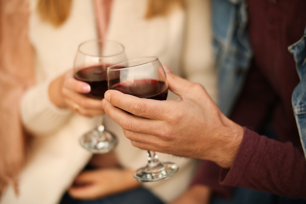 Deux verres de vin rouge gros plan dans les mains à l'extérieur de la maison. L'homme et la femme font le tintement des verres.