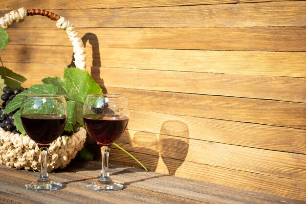 Deux verres de vin rouge et un panier de raisins sur un fond en bois