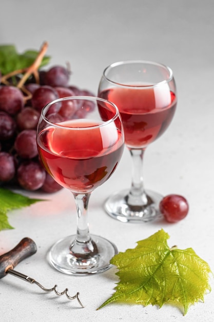 Deux verres de vin rouge ou rose une grappe de raisins rouges et tire-bouchon nature morte sur fond gris clair Célébration pour deux concept