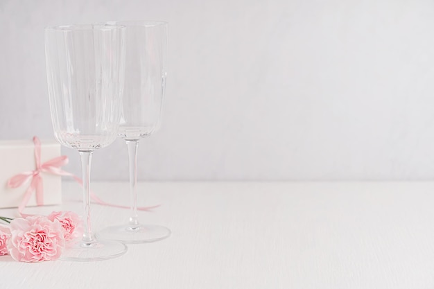 Deux verres de vin vides servis sur une table en bois blanc avec un espace de copie avec une boîte-cadeau pour un déjeuner romantique