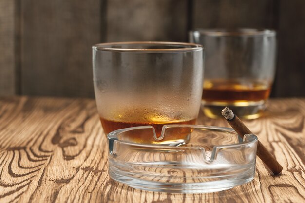 Deux verres de whisky avec un cendrier vide sur table en bois