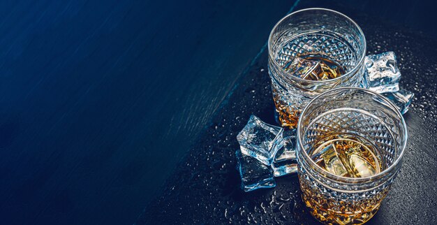 Deux verres de whisky coûteux avec de la glace sur un plateau en pierre noire