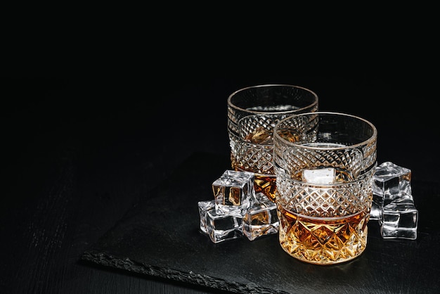 Deux verres de whisky coûteux avec de la glace sur un plateau en pierre noire
