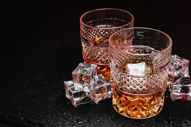 Deux verres de whisky coûteux avec de la glace sur un plateau en pierre noire