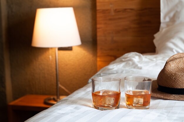 Photo deux verres de whisky avec de la glace sur le lit et une lampe d'éclairage en arrière-plan