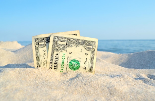 Deux vieux billets d'un dollar dans le sable sur fond de ciel bleu de la mer en été ensoleillé