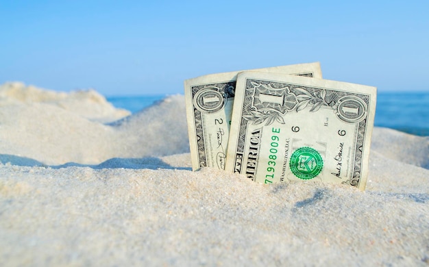 Deux vieux billets d'un dollar dans le sable sur fond de ciel bleu de la mer le jour d'été ensoleillé Gros plan de dollars sales L'argent pousse à partir de sable Concept abstrait argent affaires payer finances vacances repos voyages tourisme