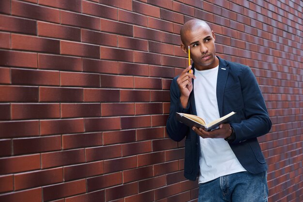 Développement du cerveau jeune homme debout sur un mur de lecture de livre touchant la tête avec un crayon pensant