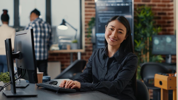 Développeur de logiciels de base de données asiatique souriant écrivant du code de programmation sur un clavier d'ordinateur assis au bureau dans une agence de développement de logiciels. Sympathique programmeur cloud innovant en matière de cybersécurité.