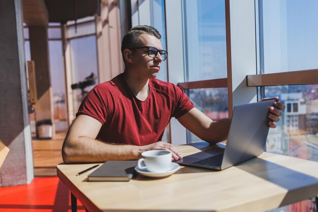 Développeur de logiciels intelligents assis au bureau dans un espace de coworking avec un ordinateur portable et créant une idée de publication à l'aide d'un netbook pour la messagerie et la mise en réseau pendant le travail indépendant