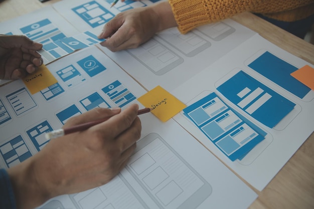 Développeur ux en gros plan et concepteur d'interface utilisateur remue-méninges sur la conception filaire de l'interface d'application mobile sur table avec breif client et code couleur au bureau moderneAgence de développement numérique créative