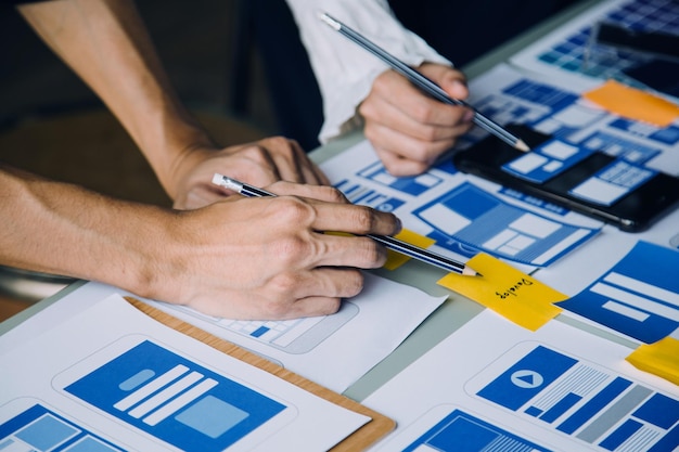 Développeur ux en gros plan et concepteur d'interface utilisateur remue-méninges sur la conception filaire de l'interface d'application mobile sur table avec breif client et code couleur au bureau moderneAgence de développement numérique créative