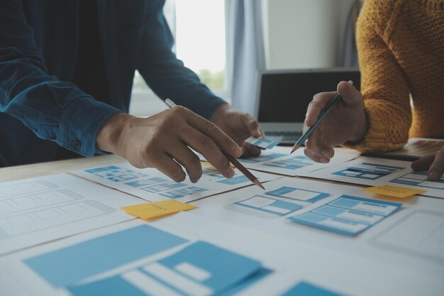 Développeur ux en gros plan et concepteur d'interface utilisateur remue-méninges sur la conception filaire de l'interface d'application mobile sur table avec breif client et code couleur au bureau moderneAgence de développement numérique créative