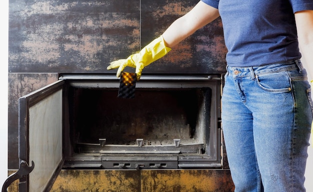 Photo devoir une femme en jeans bleus gants jaunes sur ses mains nettoie le verre résistant à la chaleur de la cheminée closeup sur les mains