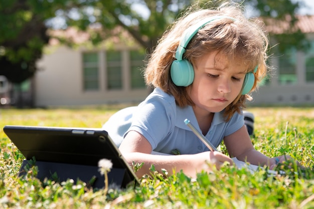 Devoirs de l'enfant à l'extérieur dans la cour de l'école petit élève d'écolier avec tablette dans le parc sur l'herbe auto e