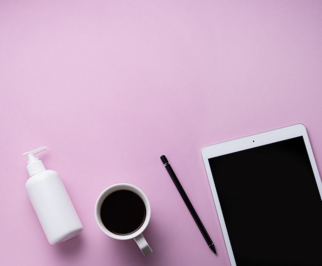 Devoirs. Mise à plat d'affaires avec une tasse de café, un désinfectant et une tablette sur fond rose