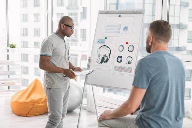 Diagnostic médical. Médecin qualifié sérieux regardant le tableau blanc tout en parlant à son patient