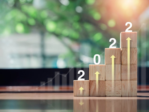 Diagramme et graphique de croissance. Flèche vers le haut rougeoyante sur le dessus des étapes du graphique des blocs de bois sur un bureau en bois, l'année 2022, style écologique. Le processus de croissance des entreprises, la finance et le concept d'amélioration économique.