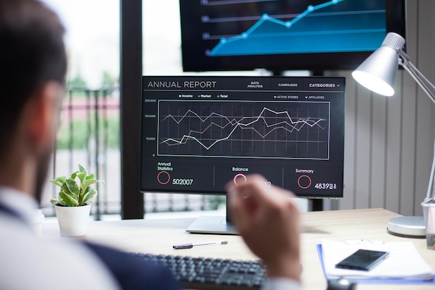 Diagrammes affichés sur un écran d'ordinateur analysés par un jeune homme d'affaires. Graphiques sur moniteur.