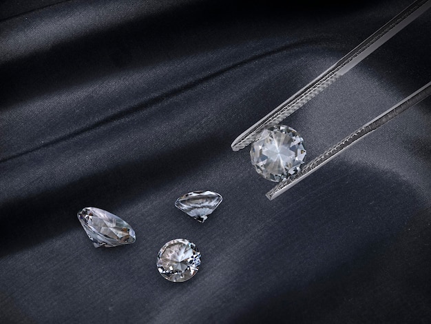 Photo diamants sélectionnés dans la pince à pierres précieuses pour fabriquer des bijoux sur fond de tissu noir