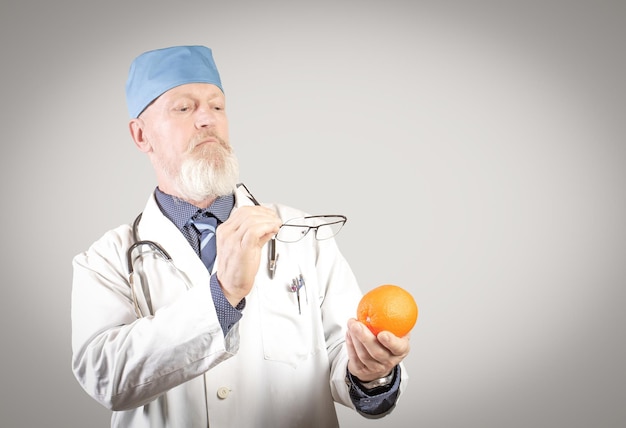Un diététicien âgé expérimenté regarde attentivement une orange à travers des lunettes